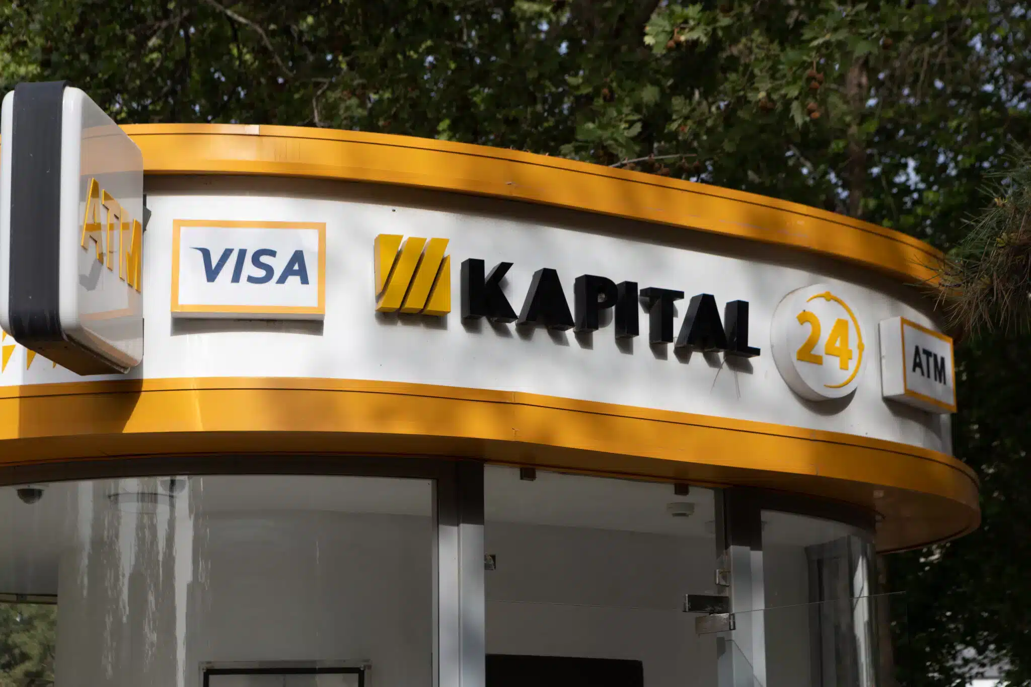 A Kapital Bank ATM in Tashkent, surrounded by green trees.